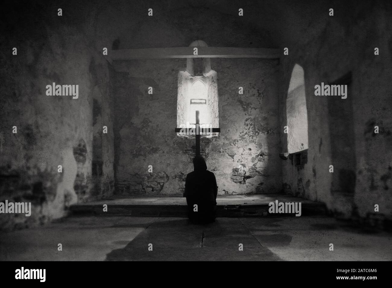 Eine Kapuzenfigur, die an einem Kreuz in einer verlassenen Kirche betet. Mit einem digitalen, lackierten Effekt und einem grunge, texturierten Schnitt. Stockfoto