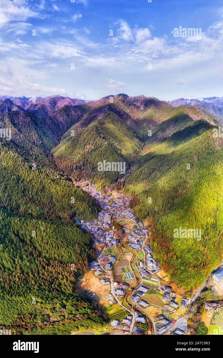Abgelegenes Bauerndorf in japanischer Bergvilllage entlang des Tals, umgeben von Pinienwäldern. Vertikales Luftpanorama. Stockfoto