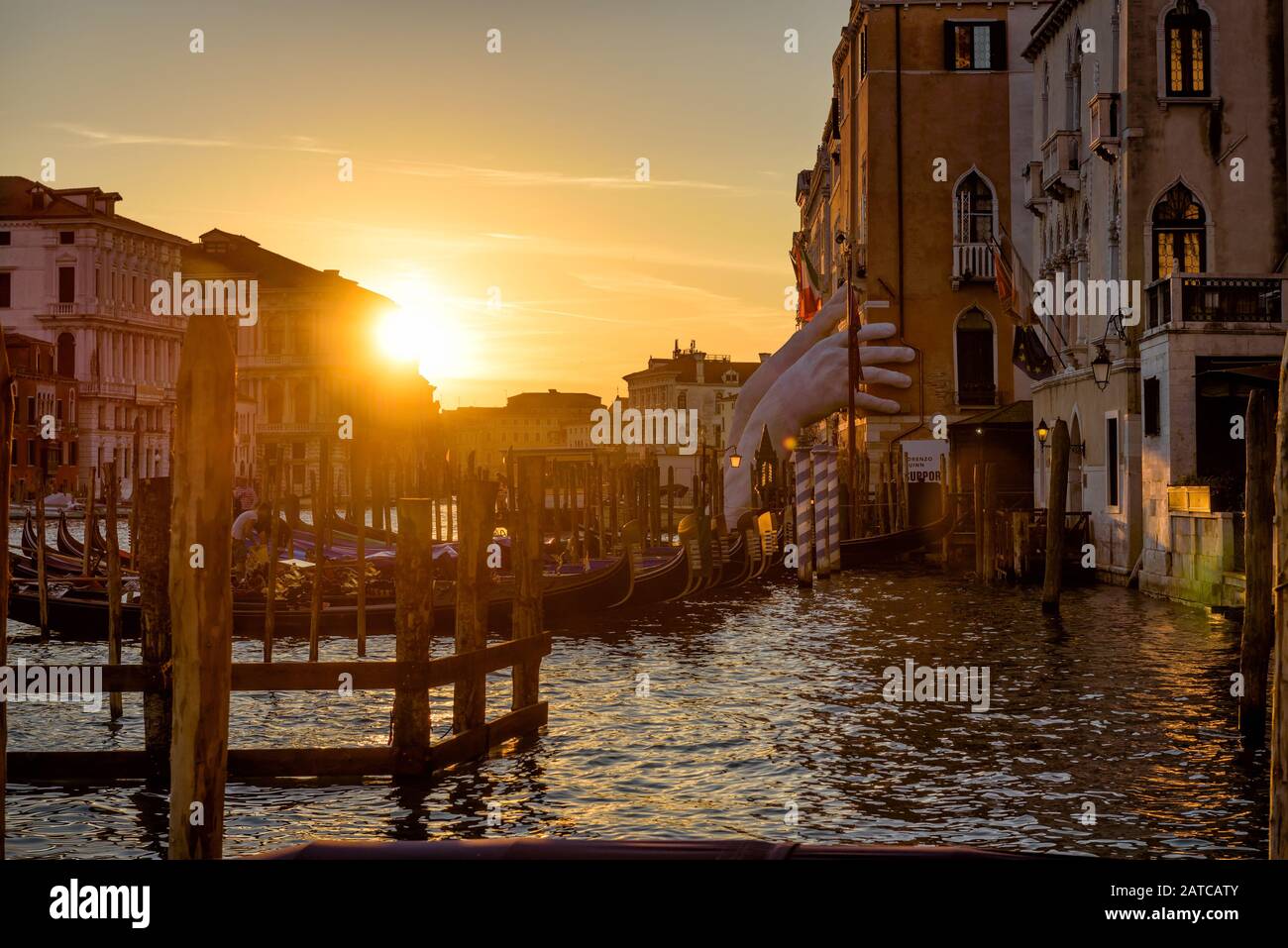 Venedig, Italien - 18. Mai 2017: Canal Grande mit Pier für Gondeln bei Sonnenuntergang. Riesige Hände, die das Gebäude stützen, sind eine Skulptur des Künstlers Lorenz Stockfoto