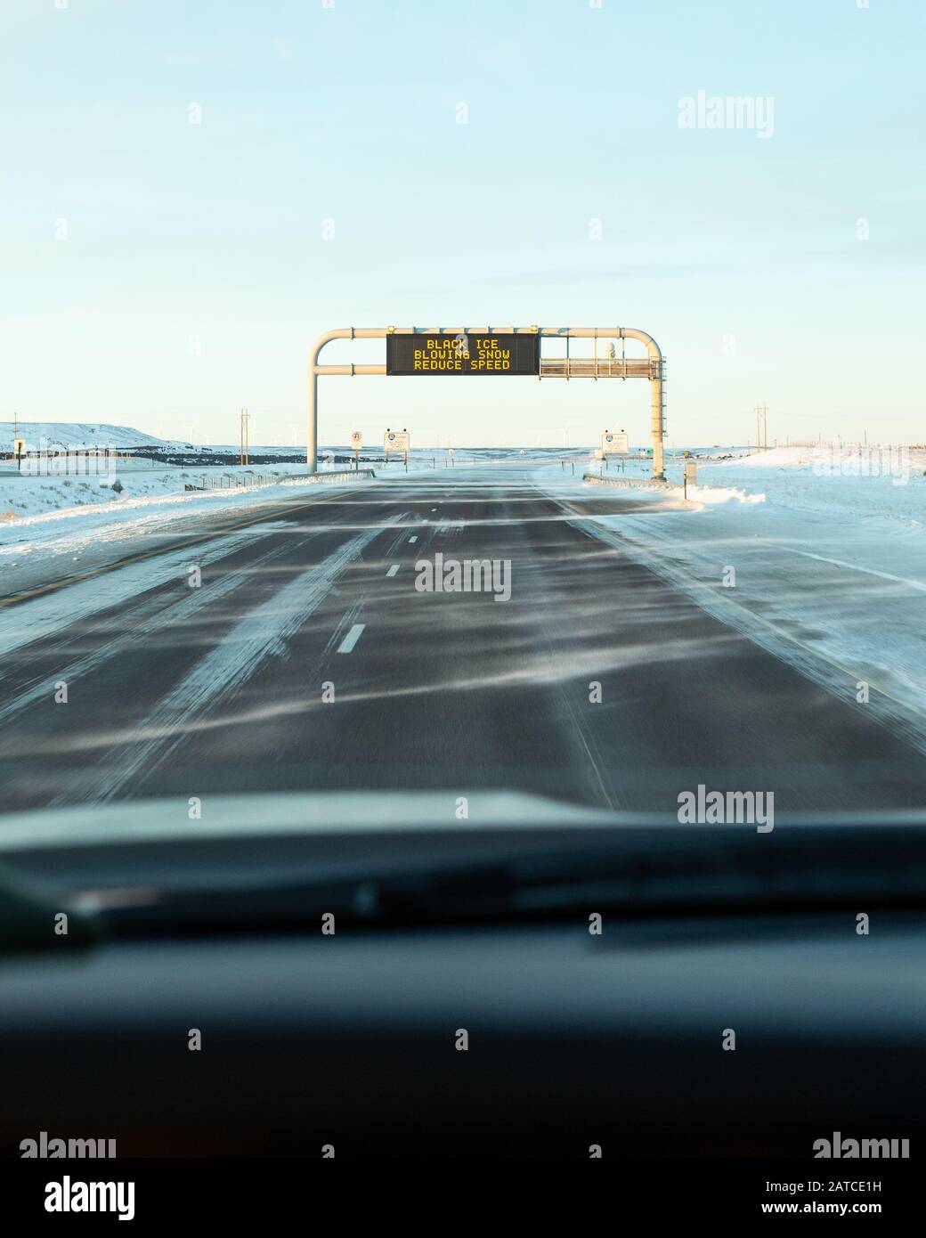 Auto fährt auf ein Straßenschild, das vor schwarzem Eis und wehendem Schnee warnt, USA Stockfoto