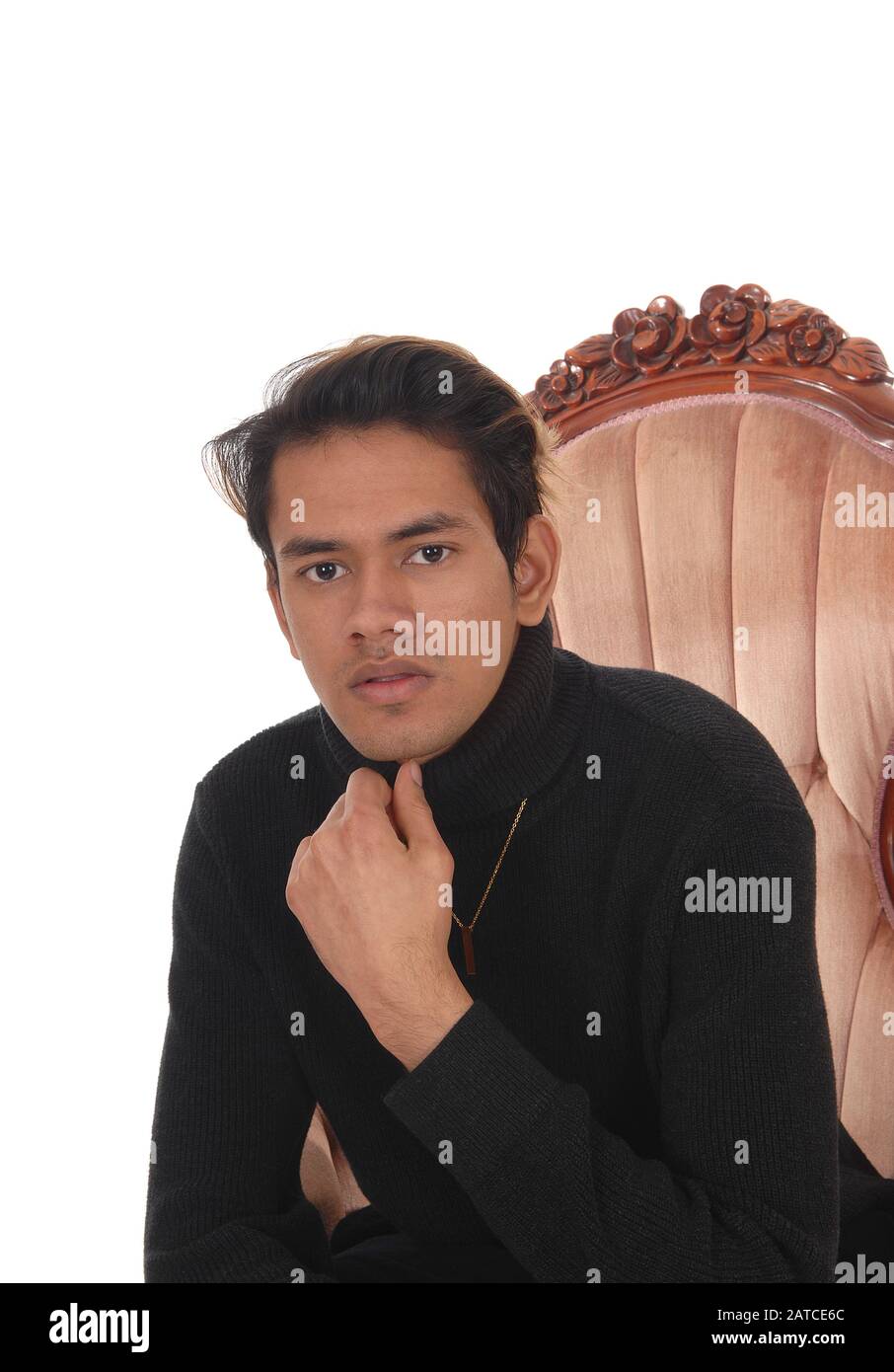 Ein Nahbild eines jungen, gut aussehenden Mannes in einem schwarzen Pullover, der in einem Sessel sitzt, isoliert für weißen Hintergrund Stockfoto