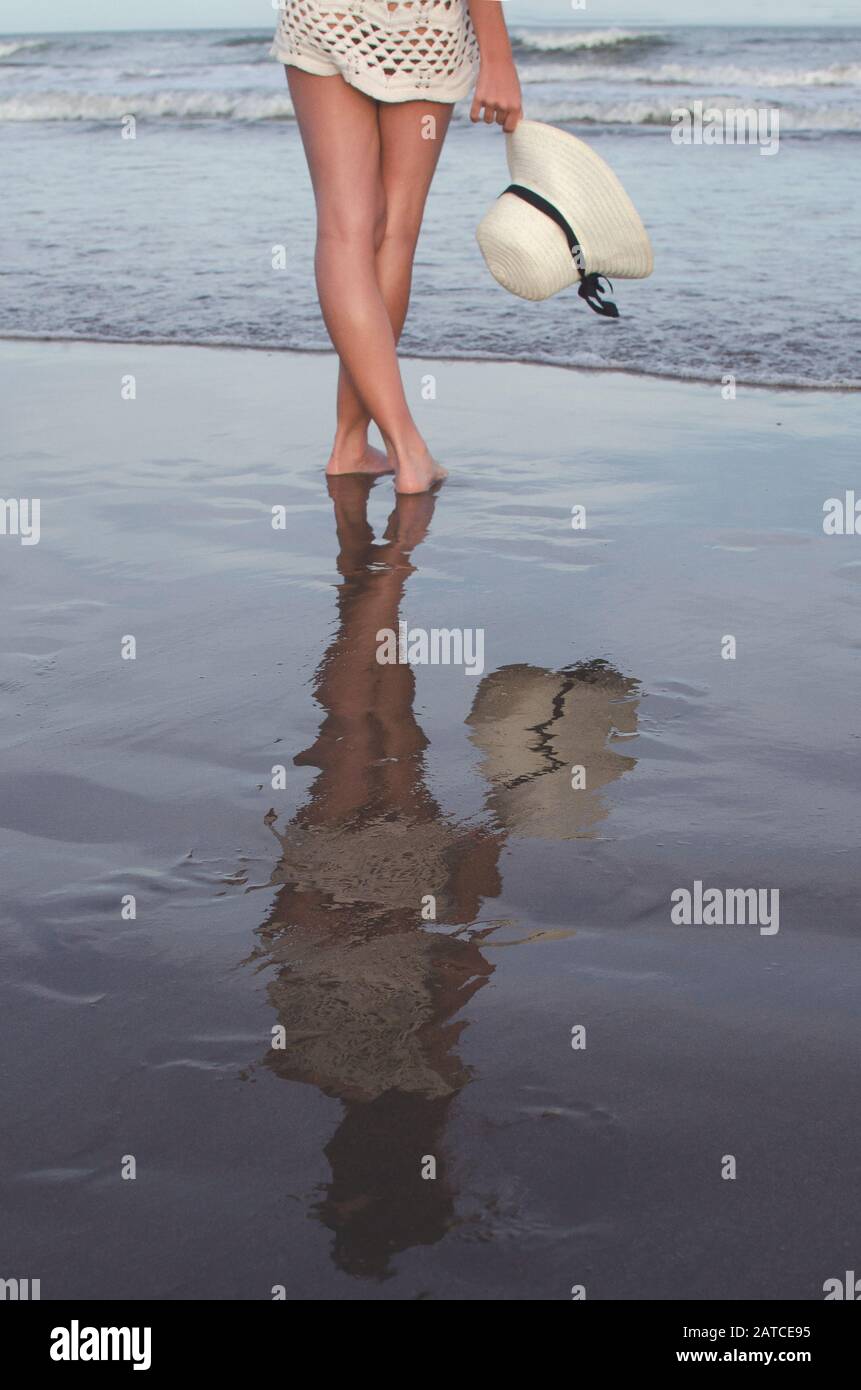 Teenager-Mädchen, das am Strand am Rande des Wassers steht und einen Sommerhut hält, Argentinien Stockfoto