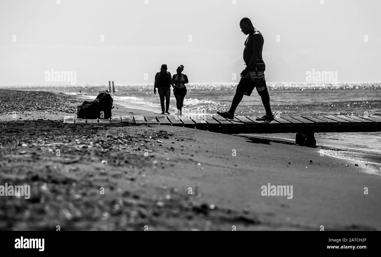 Dramatisches Schwarz-Weiß-Bild von Menschen auf einem Dock und am Strand an der karibischen Küste. Stockfoto