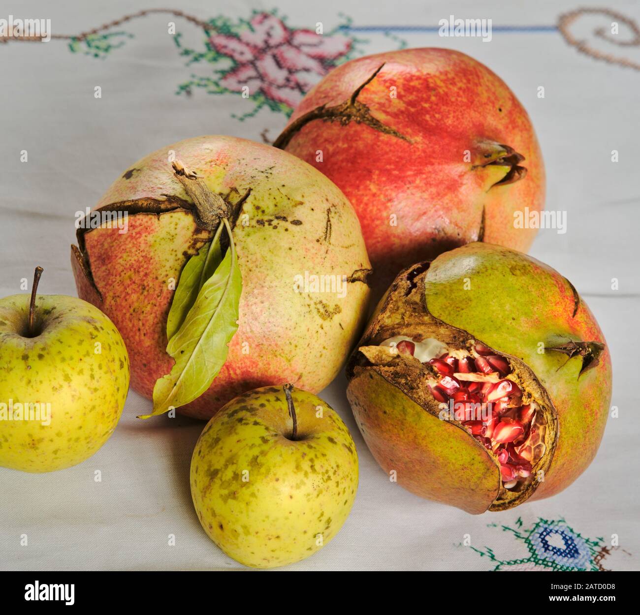 Nahaufnahme der Früchte: Drei reife Granatäpfel und zwei Äpfel, offen geteilt, um die Haufen saftiger und Schmucksteinsamen auf der Innenseite zu zeigen. Stockfoto