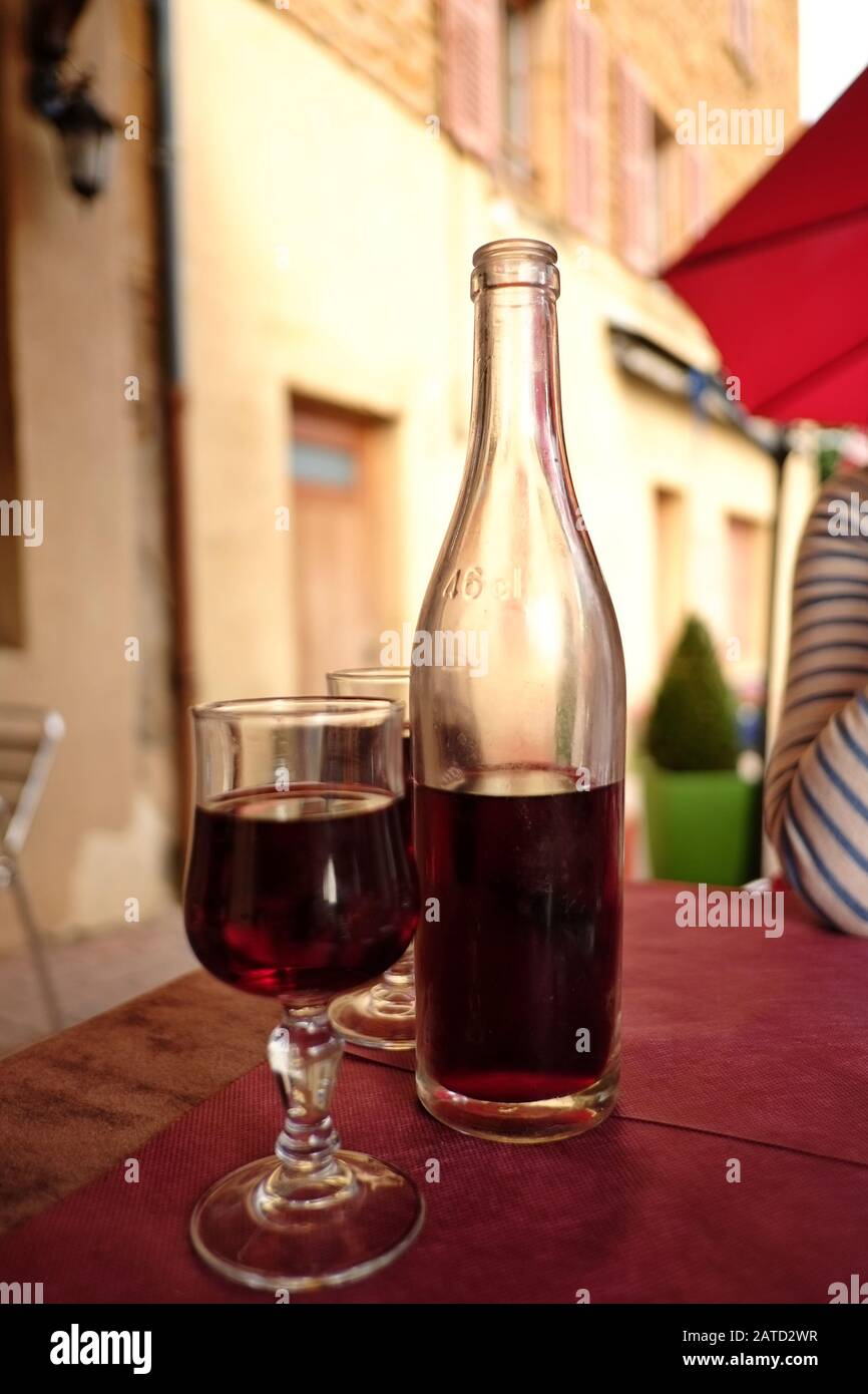 Eine klare, unbeschriftete Flasche mit lokal hergestelltem rotem Beaujolais auf einem Bistrotisch im Freien mit zwei Gläsern Wein an einem Sommertag in Bagnols Frankreich Stockfoto