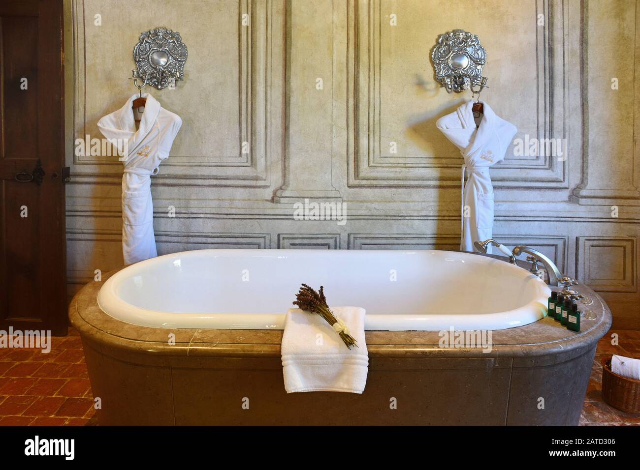 In der großen Badezimmer-Suite hängen zwei Gewänder auf silberfarbenem Kandelaber, auf dem Boden der Madame de Sévigné, Château de Bagnol eine Marmor-Surround-Badewanne. Stockfoto