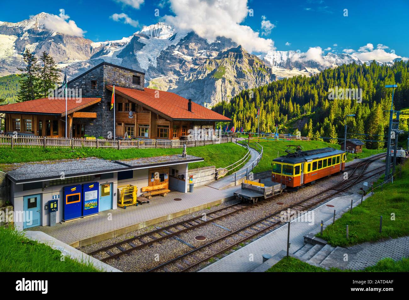 Schöner Bergbahnhof Winteregg mit gemütlichem Holzrestaurant und hohen verschneiten Bergen im Hintergrund. Touristenzug im Zug Stockfoto
