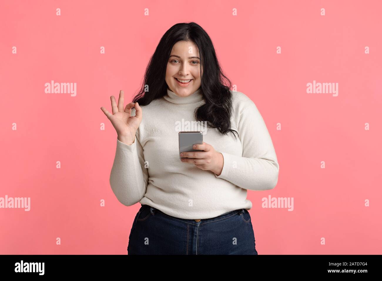 Schöne Plus Größe Model Girl Holding Smartphone Und Gesturztes Ok-Zeichen Stockfoto