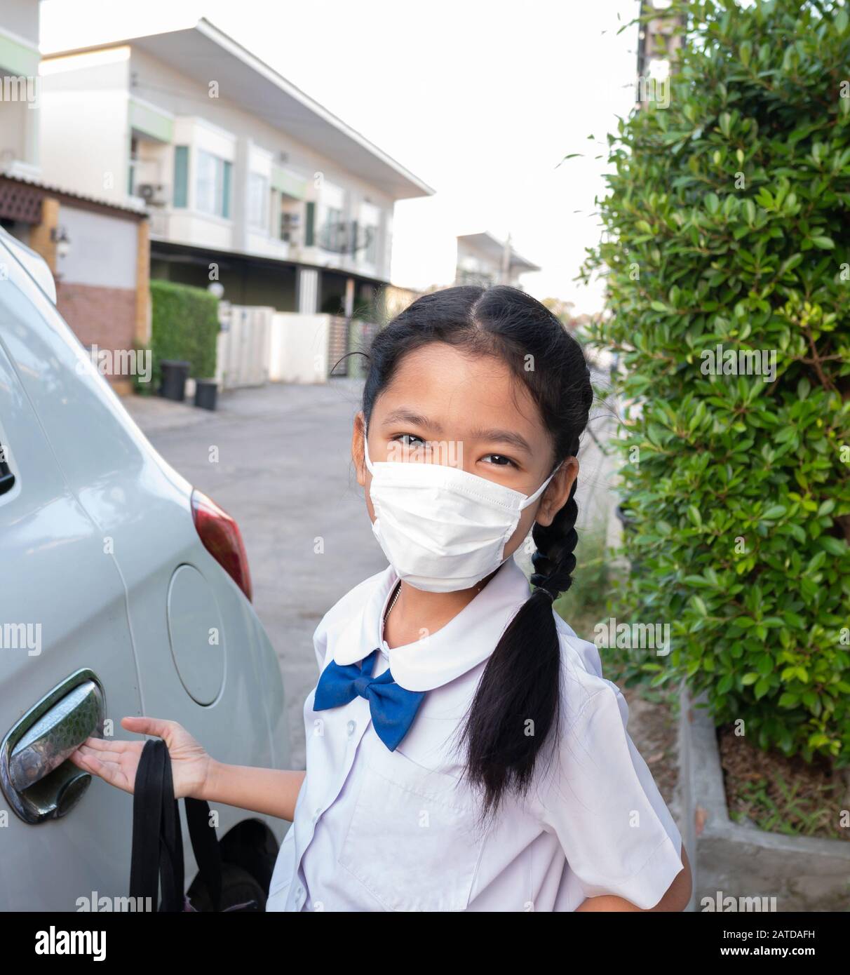 Ein kleines asiatisches Mädchen trägt eine Uniform und eine Maske, wenn es zur Schule geht, um Keime zu verhindern. Stockfoto
