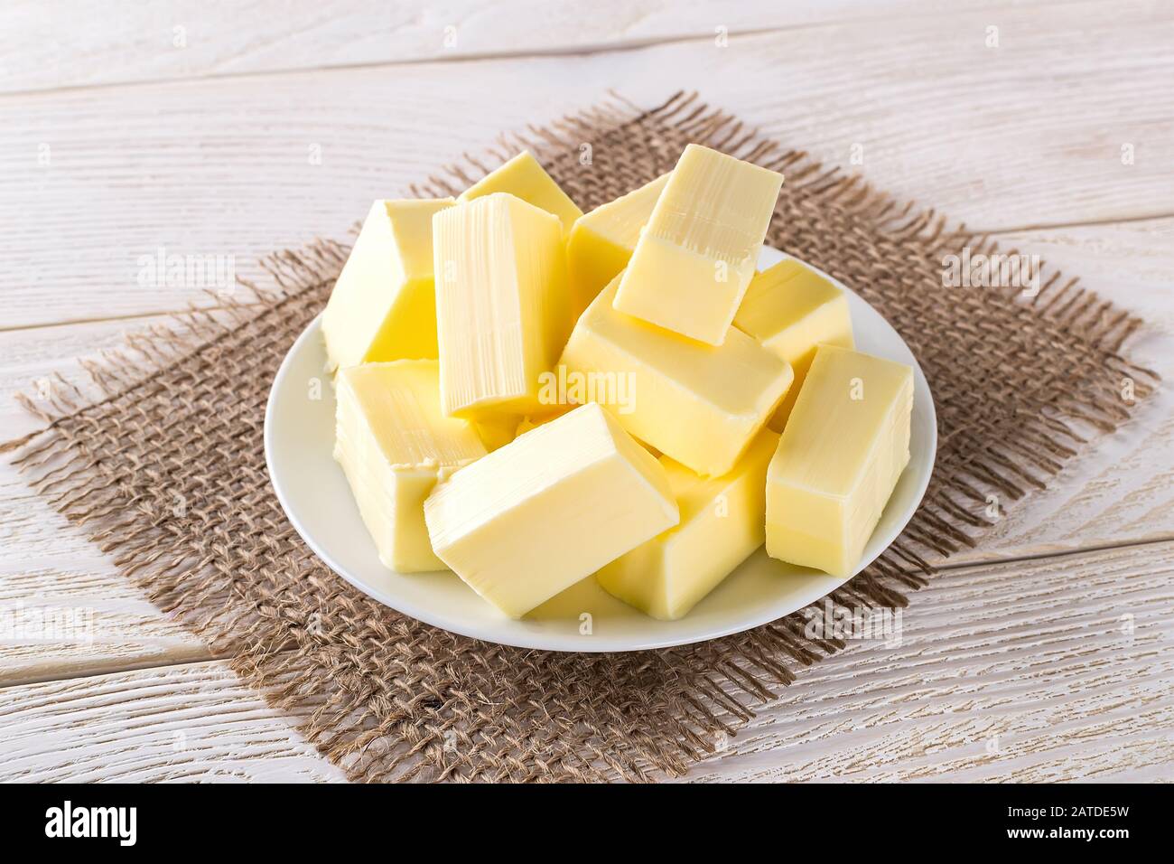 Rechteckige Stücke frische gelbe Butter auf einer weißen Untertasse über einem weißen Holztisch. Molkereiprodukte. Sandwichbutter. Natürlicher Fettnährstoff. Vorderansicht. Stockfoto