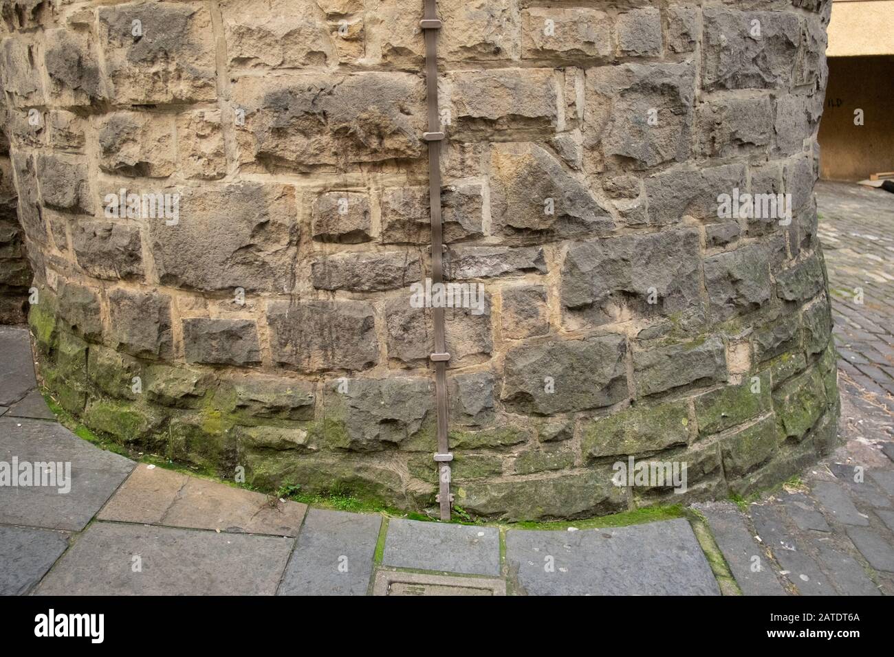 Alte gebogene Steinwand mit Blitzableiterstreifen aus Metall, Spritzspuren und grünem Schimmel, Edinburgh, Schottland Stockfoto