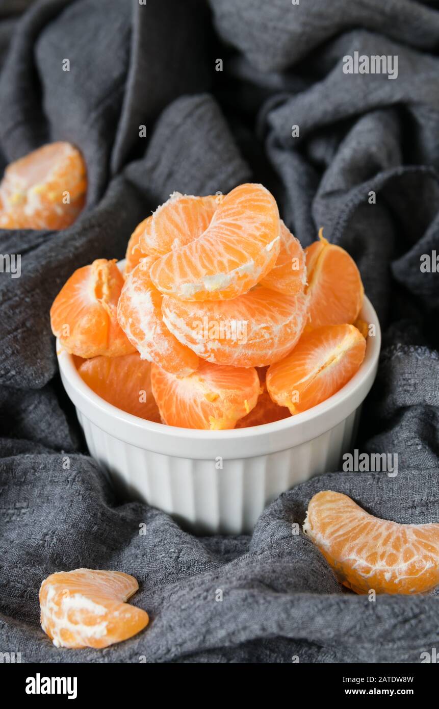 Stillleben, Scheiben reifer Mandarinen in einer weißen Platte auf einem Hintergrund aus grau drapiertem Stoff Stockfoto