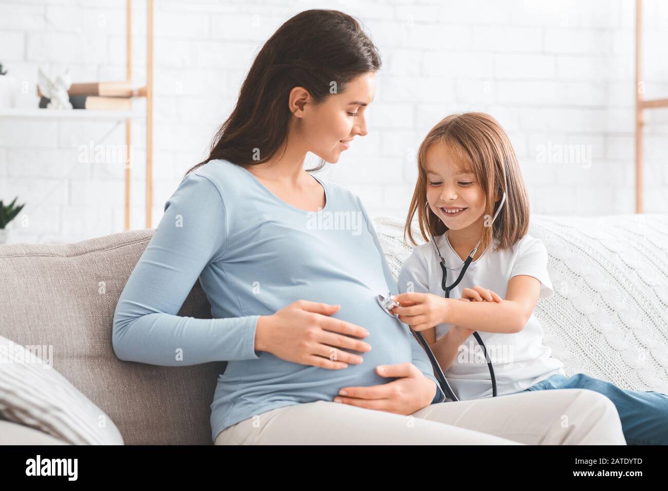 Kleines Mädchen, das Bauch ihrer schwangeren Mutter durch Stethoskop hört Stockfoto
