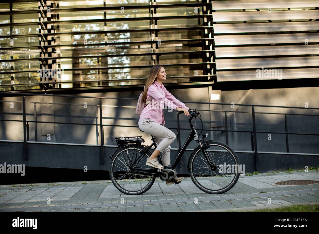 Junge Frau, die am sonnigen Tag mit dem E-Bike in städtischer Umgebung unterwegs ist Stockfoto