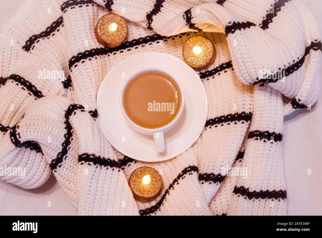 Weiße Porzellanbecher mit Kaffee mit Milch, Pullover, groben Textilien, schwarze und weiße Streifen sichere Kerzen, weißer Hintergrund. Homeless. Trend Jugend pho Stockfoto