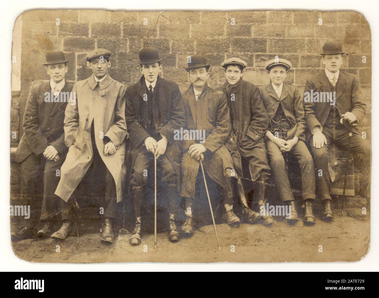 Anfang 1900 wurde die edwardianische Kabinettskarte der Gruppe von sieben jungen Männern und Jungen mit flachen Kappen und Bowler-Hüten, einige mit Wanderstöcken oder -Kähnen, abgerundeten Kragen, die zusammen sitzen, nachdem sie einen Spaziergang auf einer Bank gemacht hatten, Großbritannien Um 1905 Stockfoto