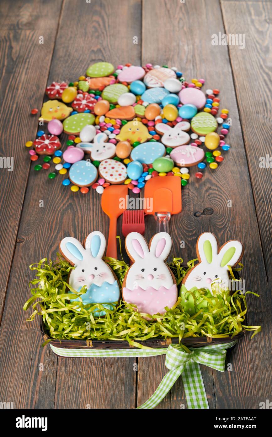 Bunte Ingwer glasierte Plätzchen auf Tisch und in Box mit Gras, Schokoladenkugeln mit Zuckerschale und Silikonspatel. Hausgemachtes, schönes Gebäck aus ostertieren, Eiern und Karotten in Kreisform. Stockfoto