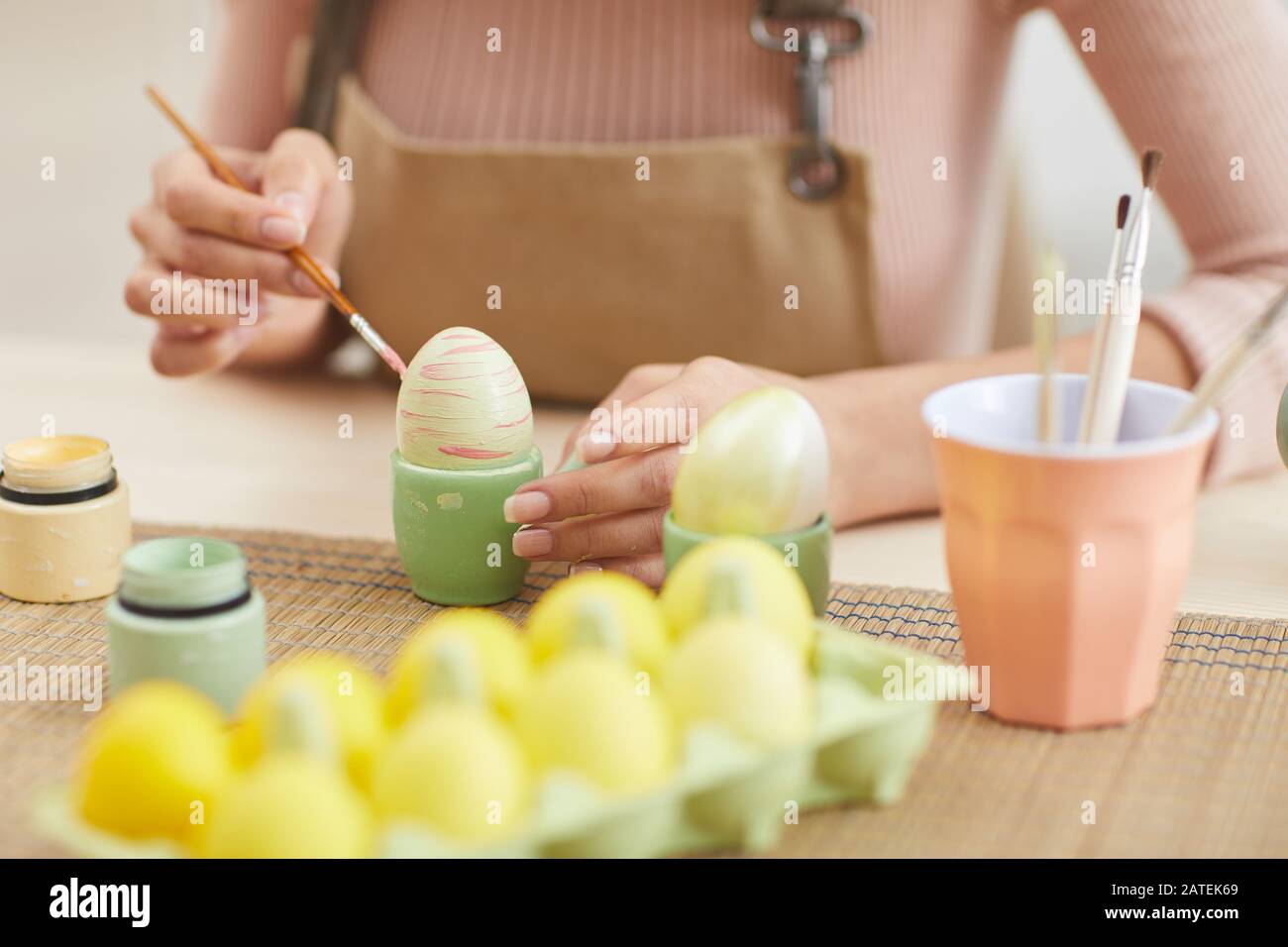 Nahaufnahme der jungen Frau, die zu Ostern Eier in Pastellfarben malt, während sie in Küche oder Kunststudio am Tisch sitzt, Kopierraum Stockfoto