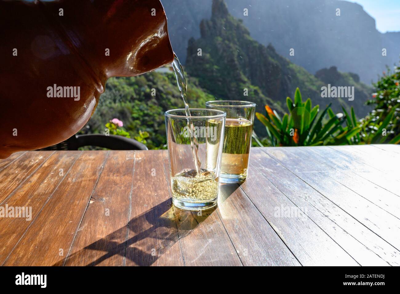 Man gießt Weißwein aus Ton Kanne in Glas auf der Terrasse mit Blick auf die grüne Landschaft der kleinen Bergdorf Masca auf Teneriffa, Spanien im sonnigen d Stockfoto