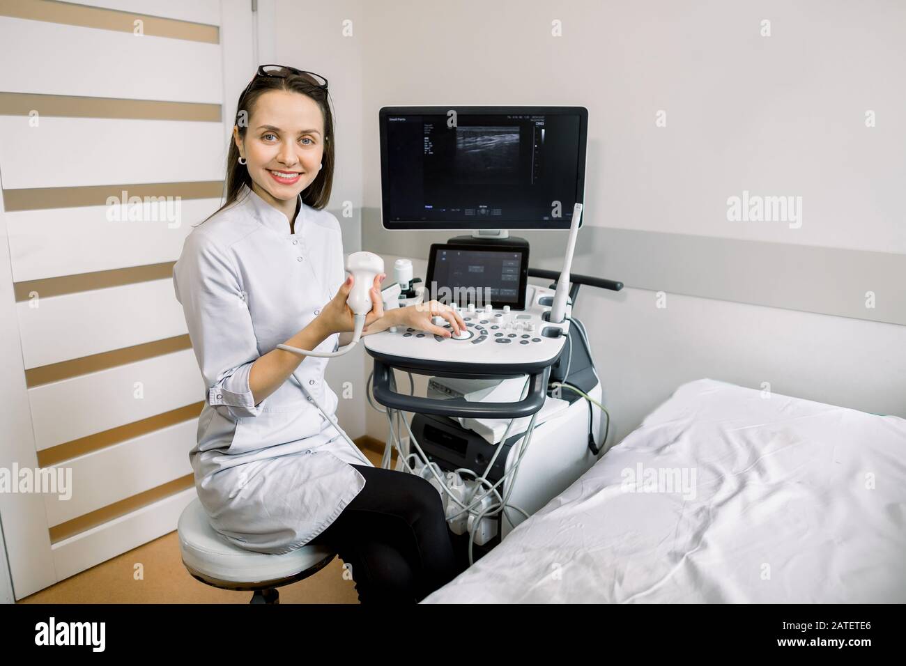 Portrait des jungen, lächelnden kaukasischen Frauenarztes, des Bedieners des 4D-Ultraschall-Scanners, des Ultraschallscanners und des Wartens auf den Patienten. Stockfoto