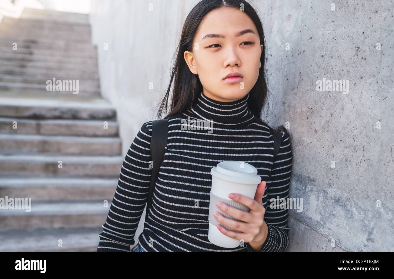 Portrait von jungen asiatischen Frau mit einem Takeaway Kaffee Tasse gegen Betongebäude. Stockfoto