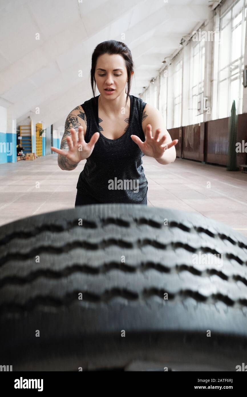 Junge kaukasische Tätowierte Sportlerin mit dunklem Haar, die einen schweren Reifen wirft Stockfoto