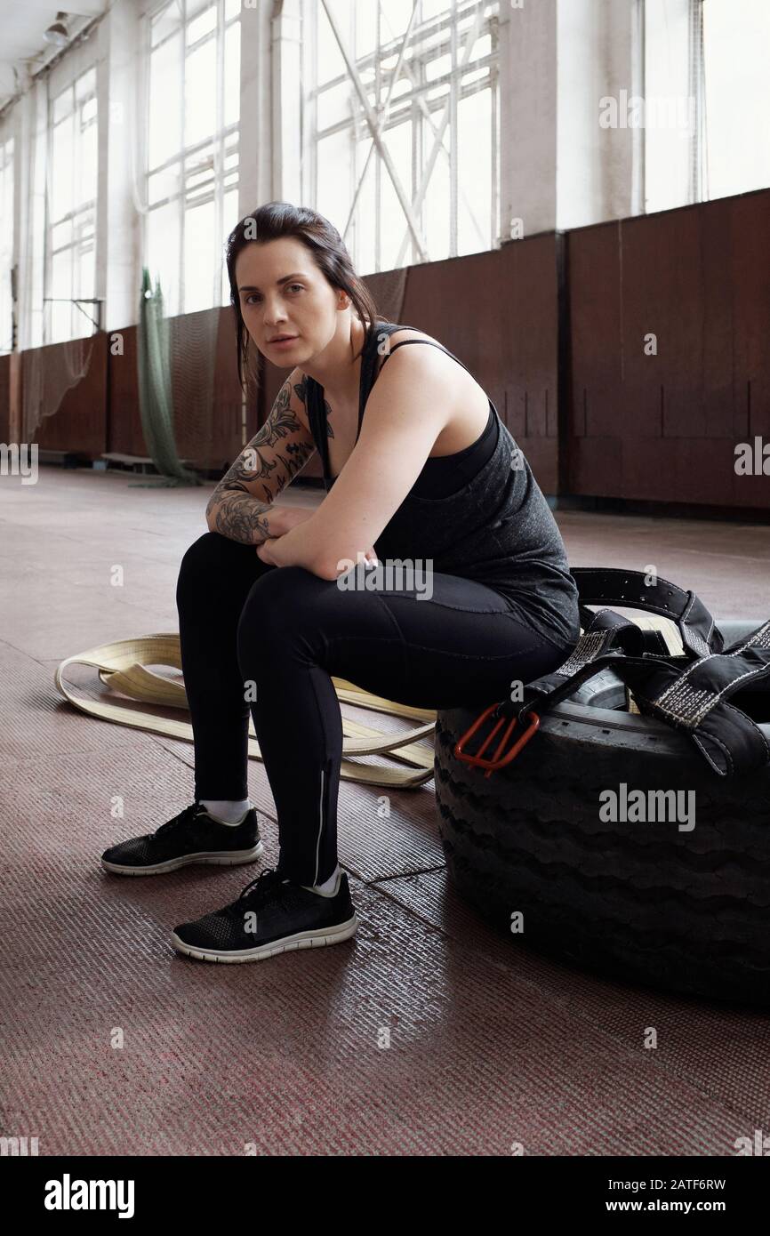 Porträt einer jungen, schönen Sportfrau mit tätowiertem Arm, der auf dem Reifen sitzt Stockfoto