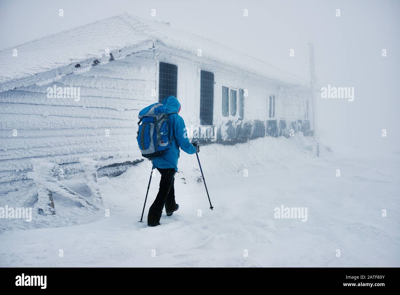 Wanderer im Winter mit Trekkking-Stöcken beim vorbeiziehen am verschneiten Gebäude Stockfoto