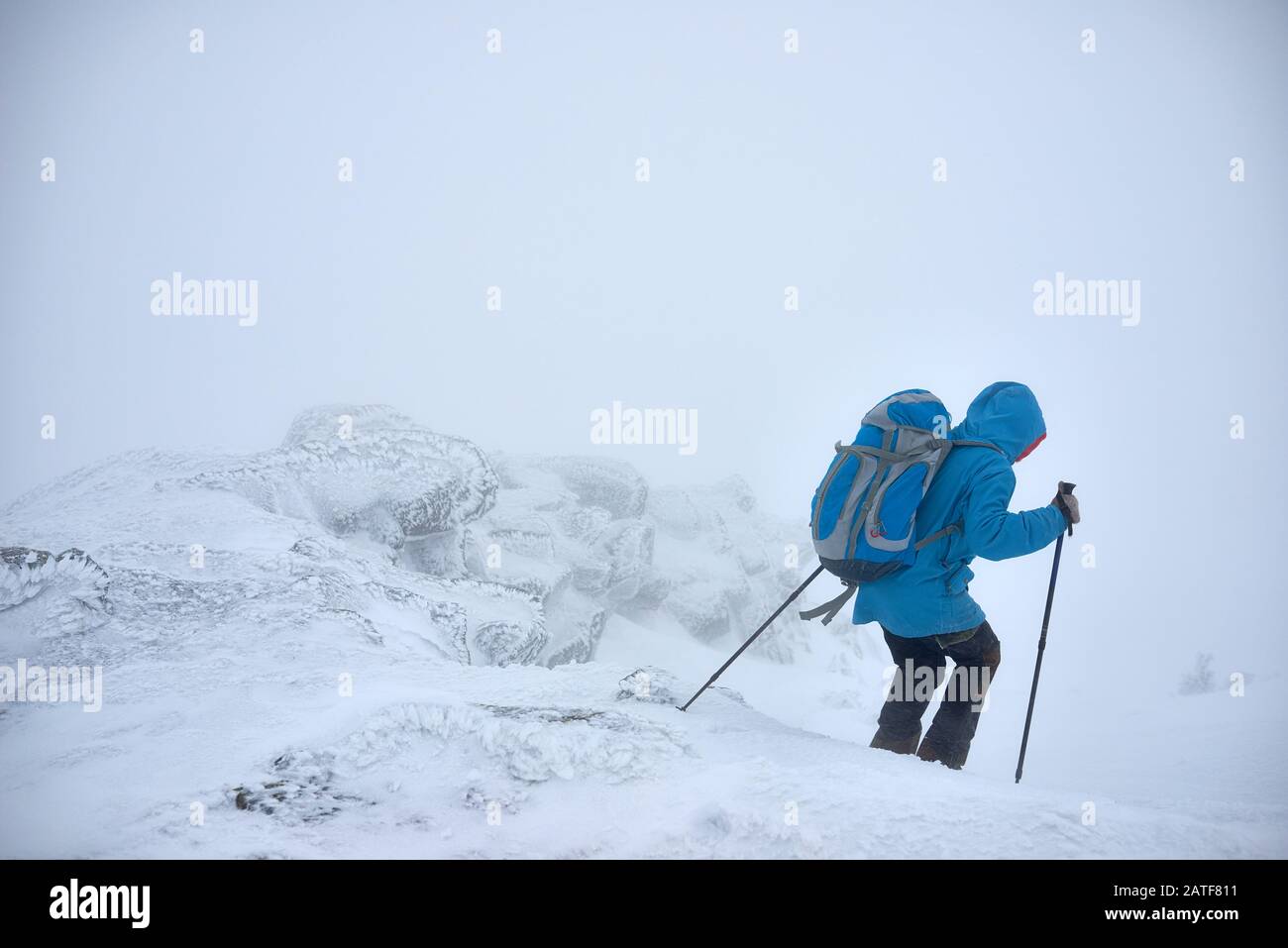 Zeitgenössischer junger Wanderer mit Trekkking-Stöcken, der im Winter unterwegs ist Stockfoto