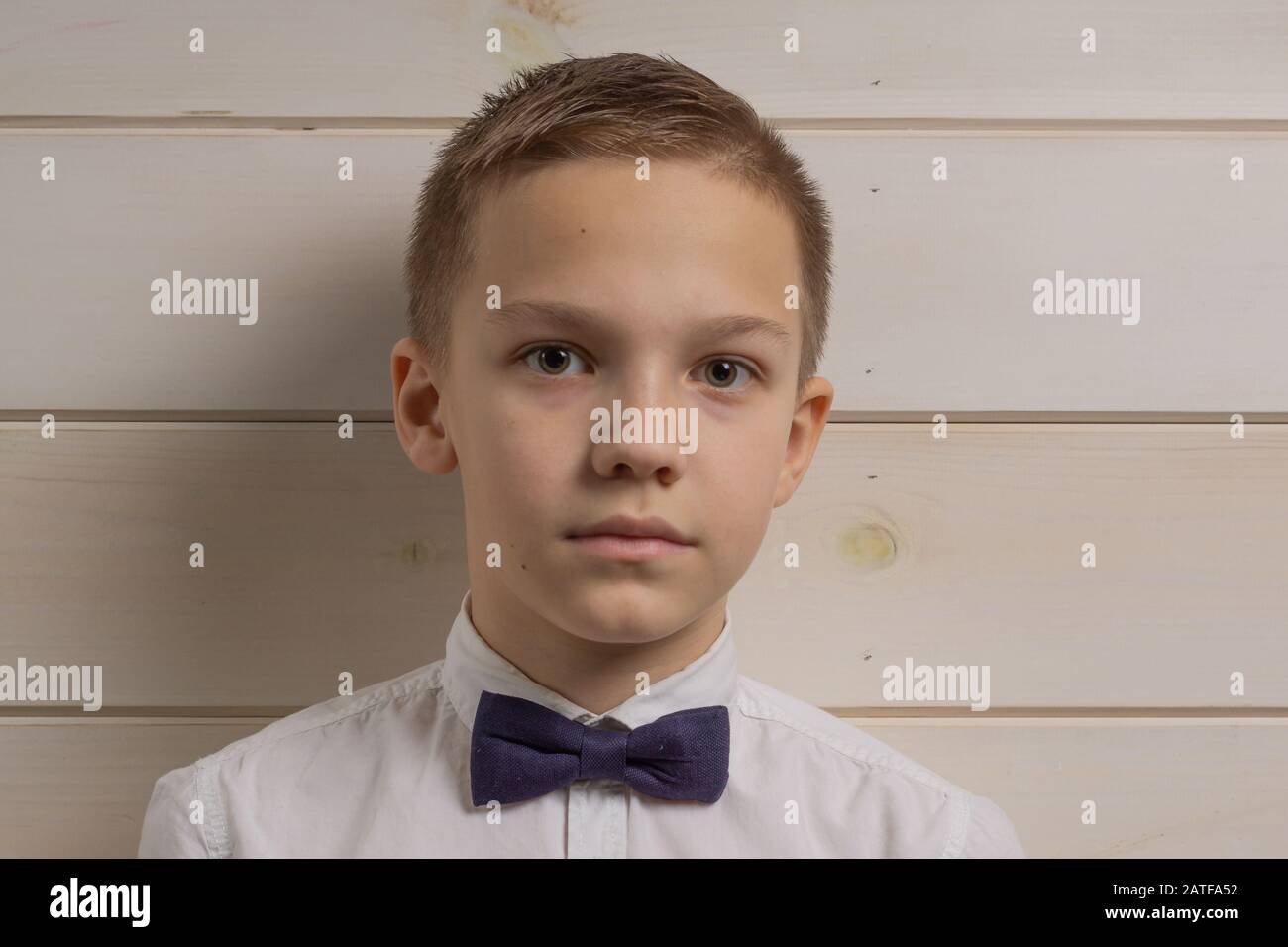 10 Jahre alter Junge mit ernsthaftem Ausdruck auf dem Hintergrund einer Holzwand Stockfoto
