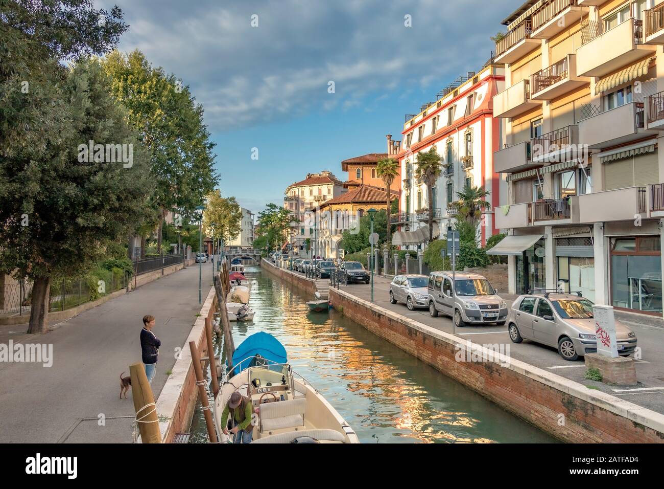 Eine Frau, die ihren Hund entlang des Kanals auf Der Via Vettor Pisani, Lido, Venedig, Italien spazieren ließ Stockfoto