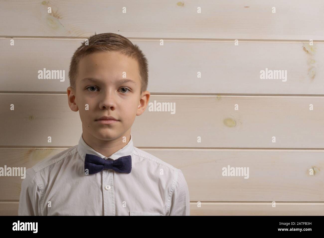 10 Jahre alter Junge mit ernsthaftem Ausdruck auf dem Hintergrund einer Holzwand Stockfoto