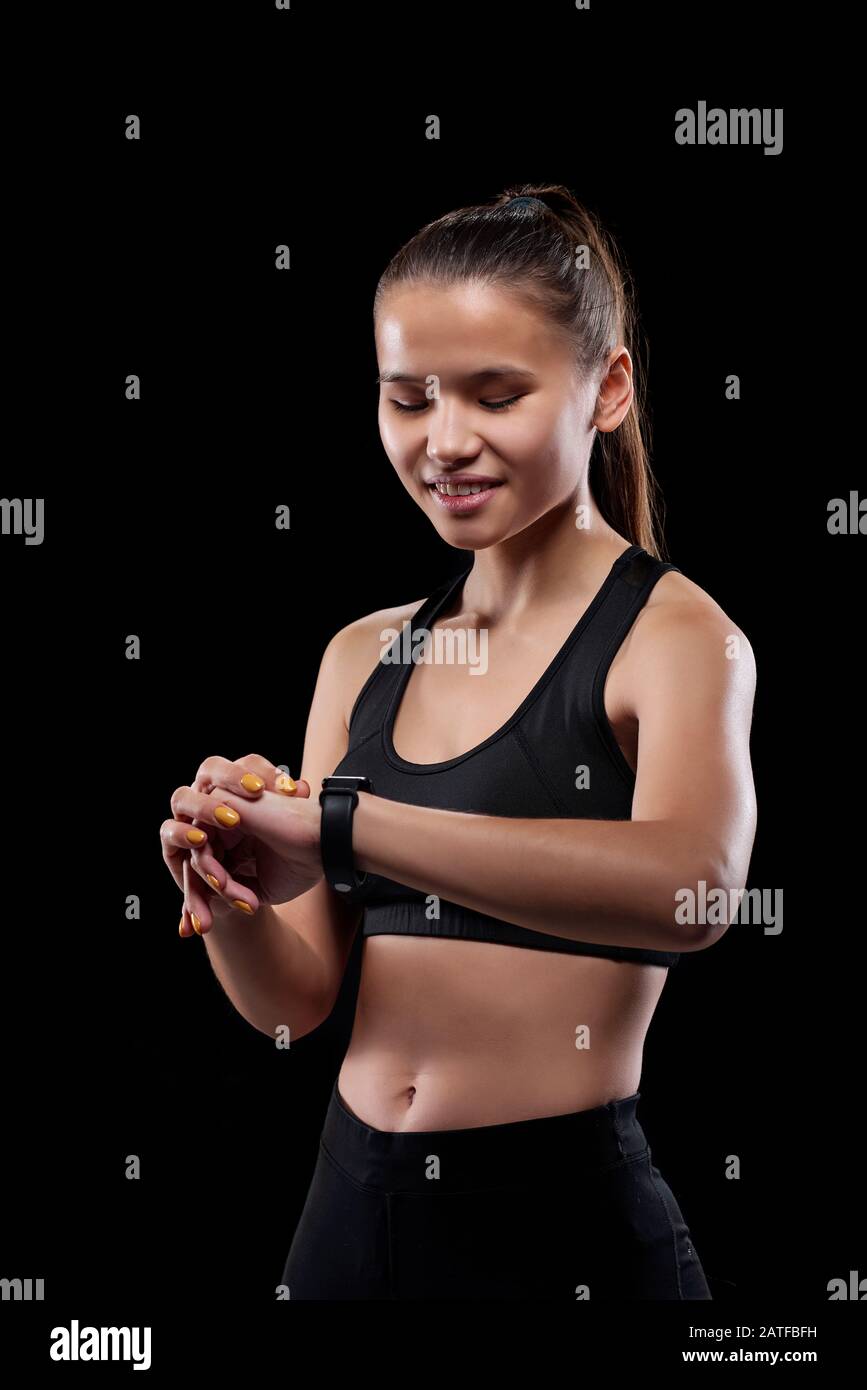 Junge lächelnde Frau, die sich während ihrer Aktivität auf ihre Armbanduhr in Isolation blickt Stockfoto