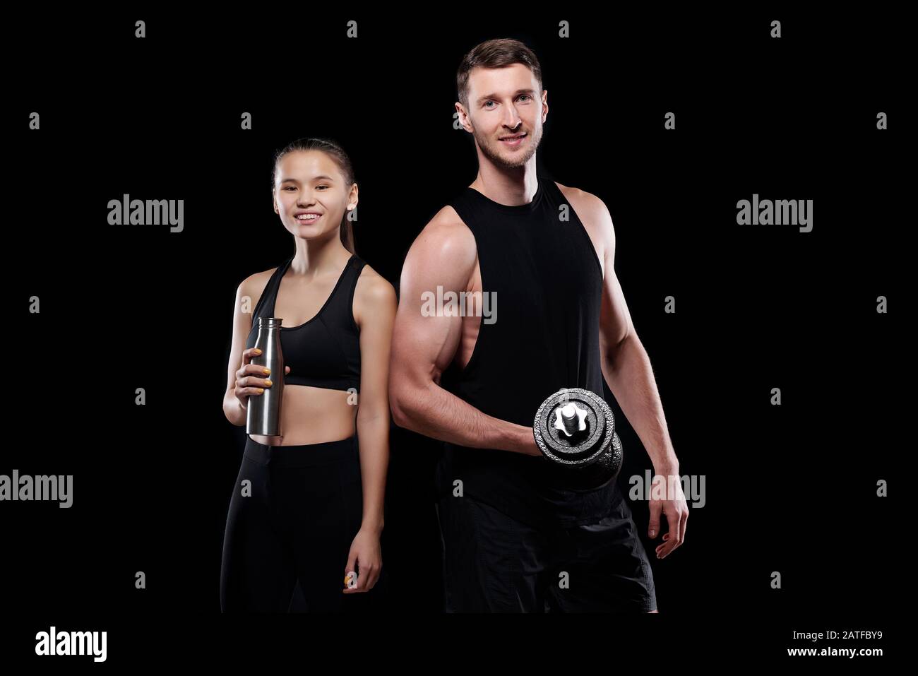 Fröhliche junge Sportlerin mit einer Flasche Wasser und muskulösem Mann mit Barbell Stockfoto