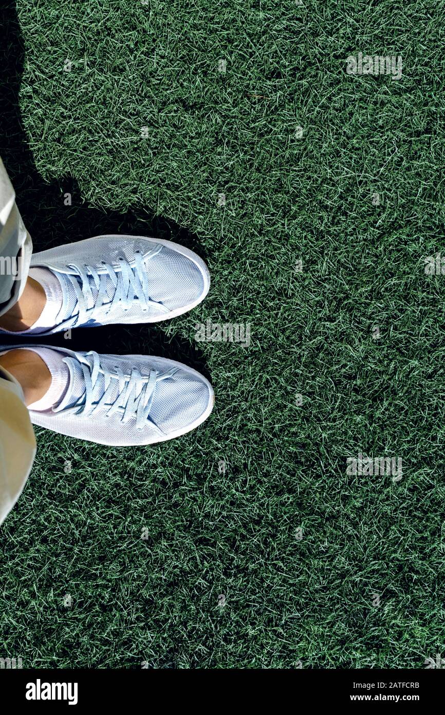 Füße in Turnschuhen stehen auf dem Gras, Draufsicht. Vertikales Foto, leere Stelle für Text. Stockfoto