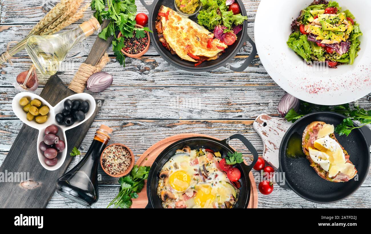 Ein Set Lebensmittel. Shakshuka, Omelette, Avocado-Salat, Sandwich mit pochiertem Ei. Auf Holzgrund. Freier Speicherplatz für Text. Draufsicht. Stockfoto