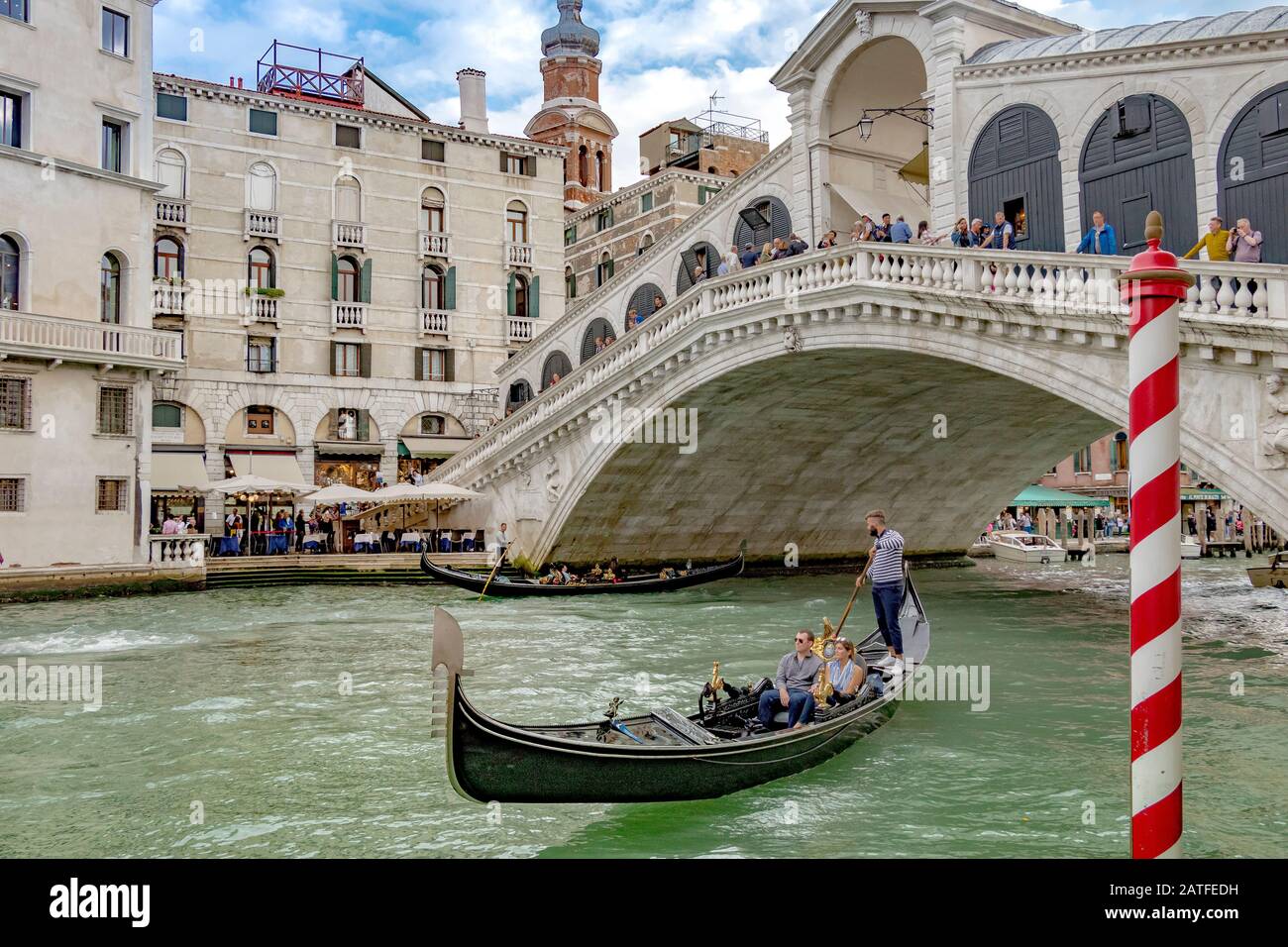 Eine Gondel mit zwei Personen, die eine Gondelfahrt vor der Rialto-Brücke machen, die älteste von vier Brücken, die den Canal Grande in Venedig, Italien, überqueren Stockfoto