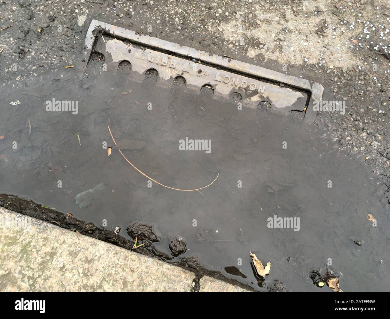 Wasserpfütze um eine alte Eisenstraße / Straßenabflussgitterabdeckung, bei der die fehlenden Wartungs- und Räumungsarbeiten die Abflüsse blockiert und das Regenwasser nicht mehr mitführen können. GROSSBRITANNIEN. Stockfoto