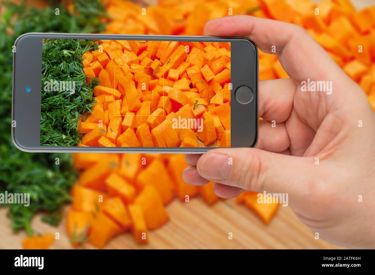 Frisches Gemüse, bevor es in die Pfanne geladen wird. Zutaten zum Kochen. Karotten auf dem Smartphone-Bildschirm. Stockfoto