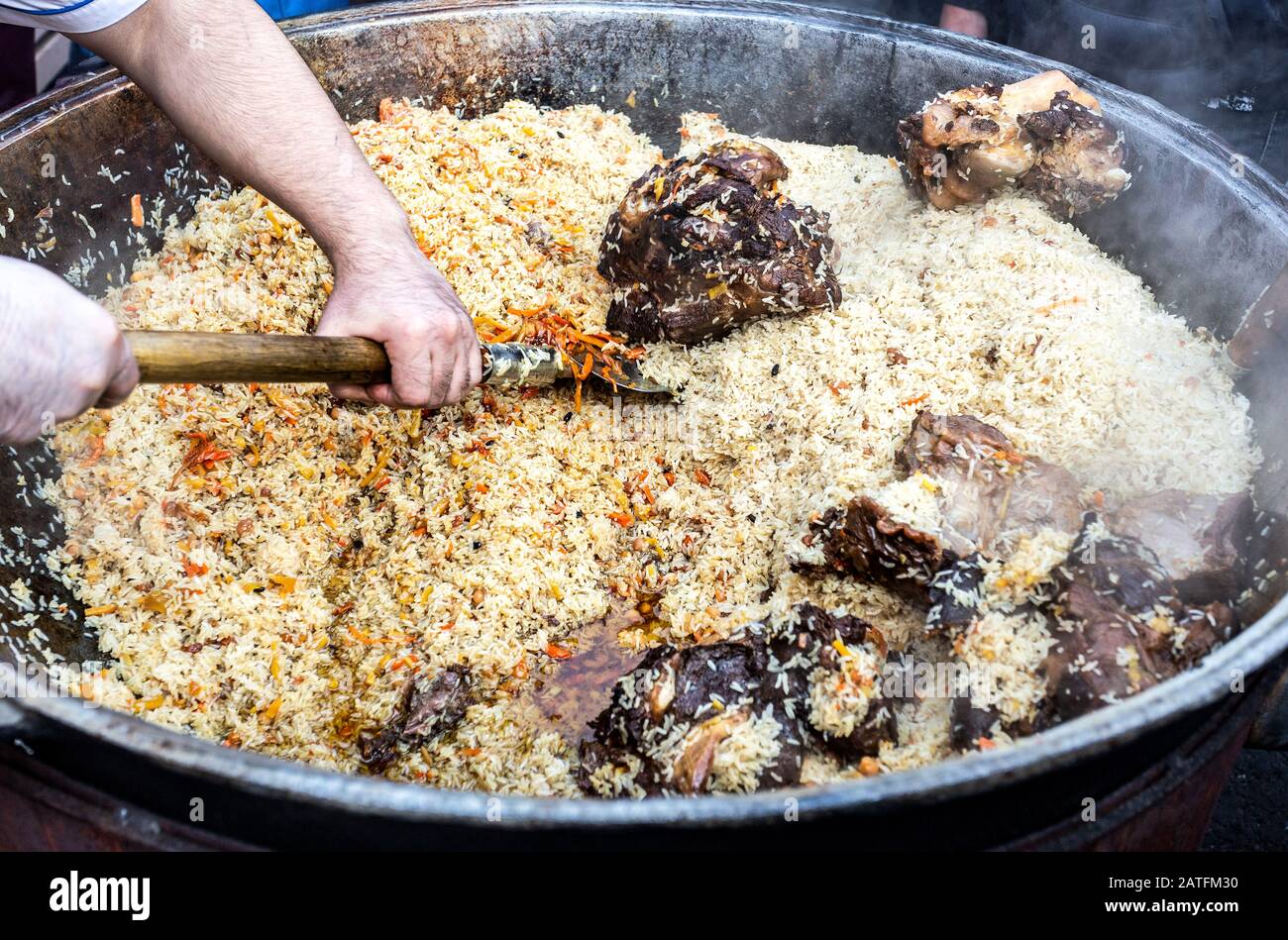 Appetitliches traditionelles usbekisches Pilaf in einem großen Kessel. Straßennahrung. Kochen im Freien Stockfoto