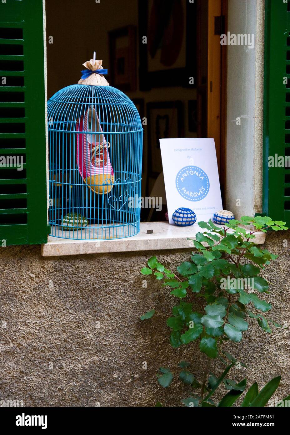 Blauer Vogelkäfig dekoriert, mit gemalten Schuh innen an rustikalem grünen Fenster. Käfig ohne Vogel im Inneren, rustikale Hausdekoration. Stockfoto