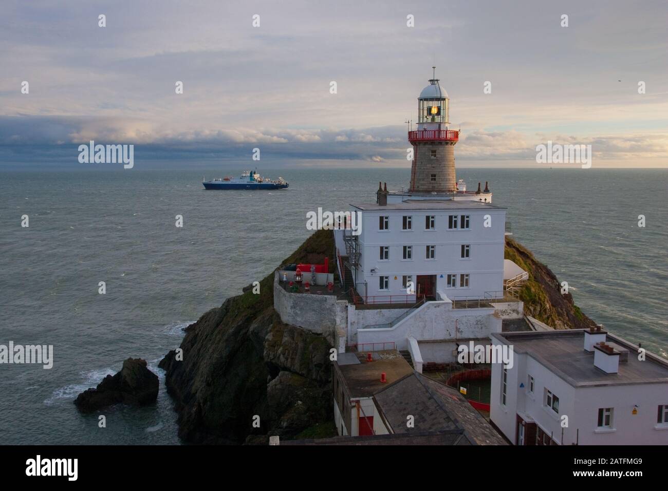 Der Baily Leuchtturm, Howth. co. Dublin, Baily Leuchtturm auf Howth Klippen, Blick auf den Baily Leuchtturm von der Klippe mit Frachtschiff im Hintergrund Stockfoto