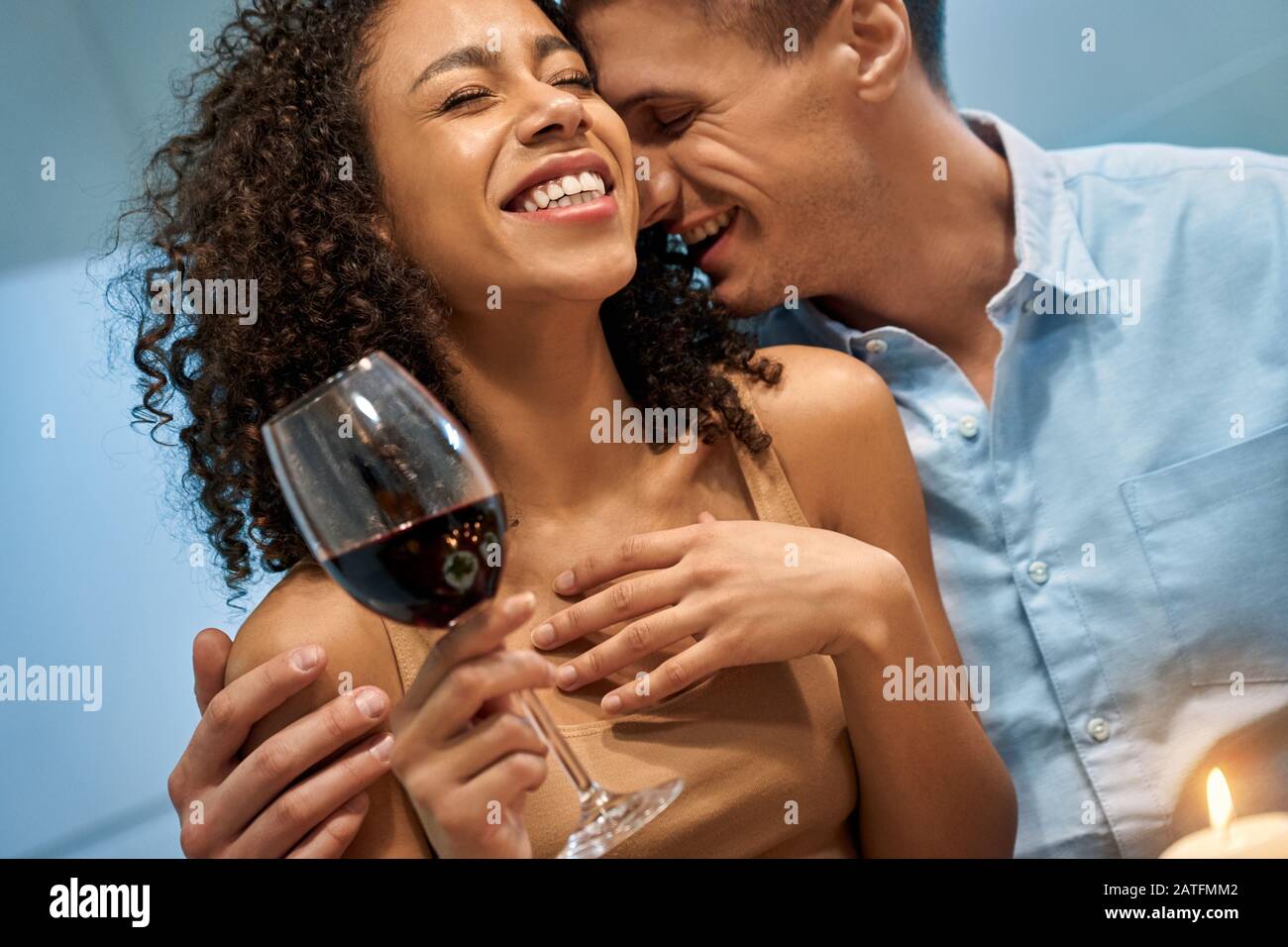 Junger Erwachsener und afro-amerikanische Frau lächeln weit und genießen ein romantisches Abendessen Stockfoto