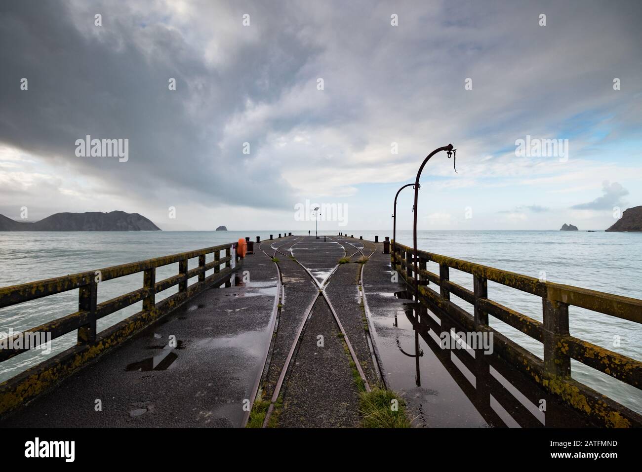 Blick von der längsten Wharf (Tolaga Bay) in Neuseeland mit dramatischen Wolken und Reflexionen in einer Pfütze entlang von Bahngleisen und Kränen. Stockfoto