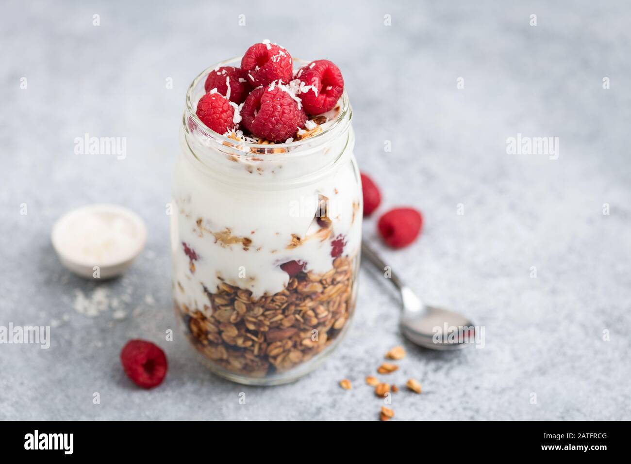 Joghurt mit Granola und Himbeeren im Mixbecher auf Betongrund. Gesundes Frühstück oder Snack für unterwegs Stockfoto