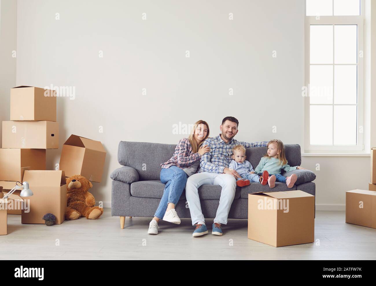 Glückliche Familie mit Kindern, die in einem neuen Mehrfamilienhaus mit Kisten umziehen. Stockfoto