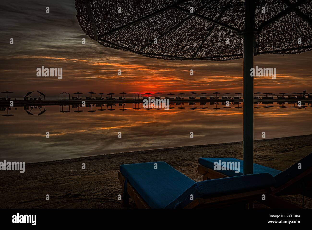 Zwei blaue Sonnenliegen und ein Regenschirm, der bei Sonnenuntergang an einem Strand im roten Meer steht, El Gouna, Ägypten, Jnuary 16, 2020 Stockfoto