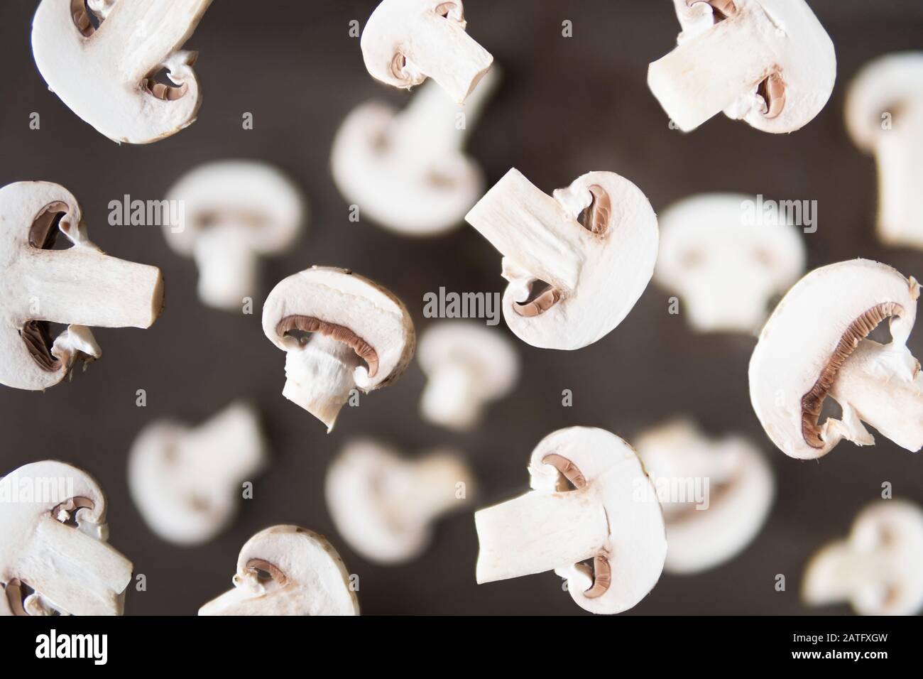 Muster von Champignonpilzen in Scheiben, die über dunkelbraunem Hintergrund levitieren Stockfoto