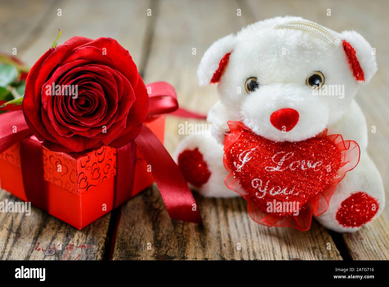 Valentinstag und Frauentagskonzept. Weißer weicher Spielzeugbär, Geschenkbox und rote Rose auf Holztisch. Selektiver Fokus. Stockfoto