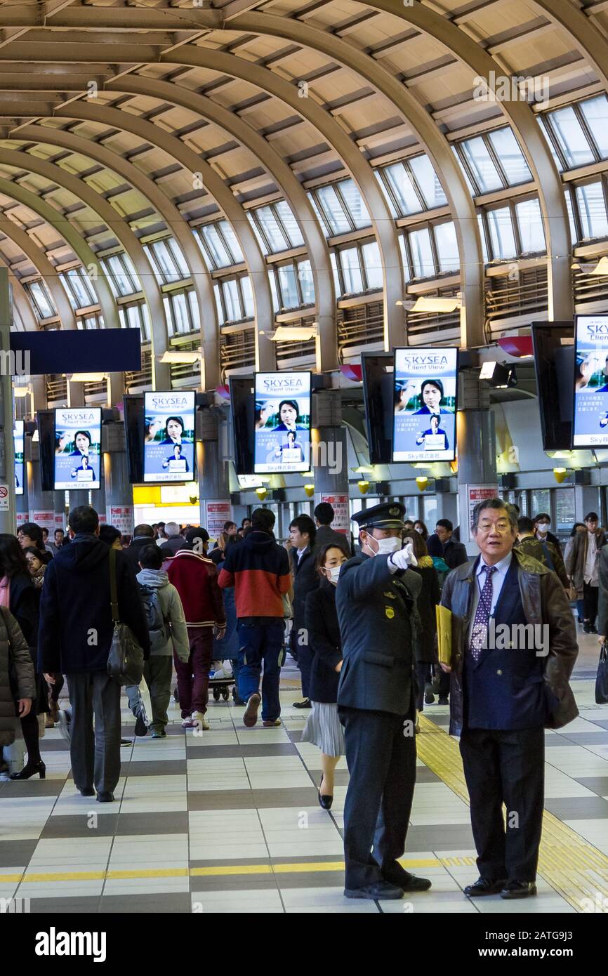 Ein Stationsmitarbeiter weist einen Salaryman in Shinagawa Station, Tokio, Japan, auf die Wegbeschreibung hin. Stockfoto